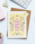 A greeting card with the words "With love and dua specially for you" placed on a brown envelope on a desk. a reflective heart-shaped sticker besides it, along with a notebook, a wrapped gift, a metal clip and a keyboard.